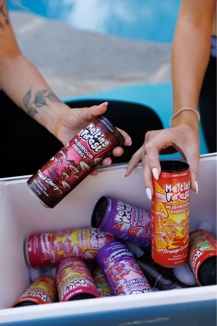 People’s hands holding mushroom drinks from a box of mushroom drinks.